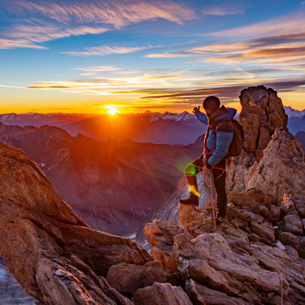 man in green jacket standing on rock formation during sunset